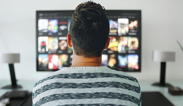 a man watching a tv with many apps including now tv